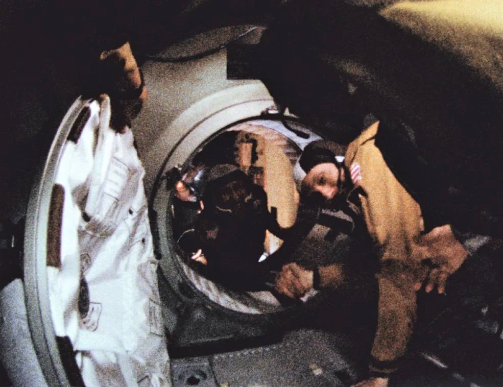 Alexei Leonov and Thomas Stafford reaching toward each other through the open spacecraft interface.