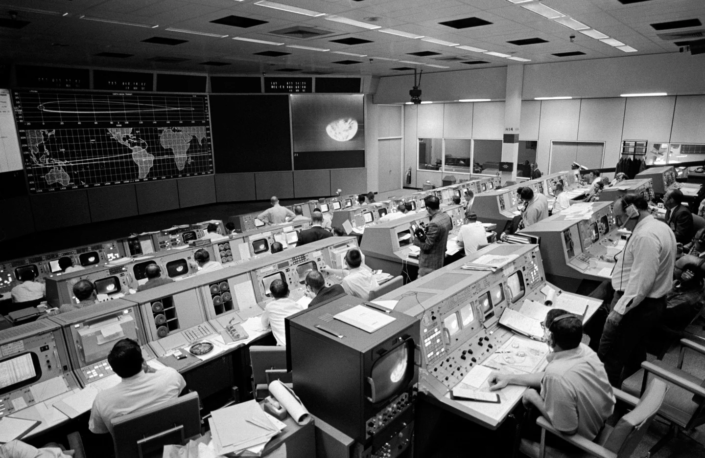 Flight controllers watch a large screen showing Earth in an Apollo 8 television transmission.
