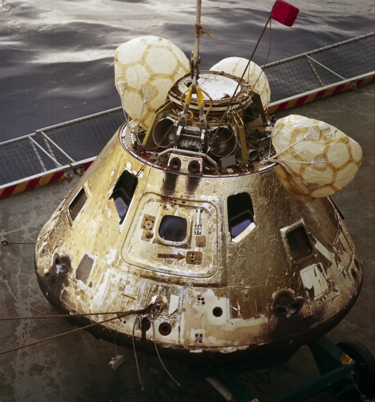 The returned Apollo 8 command module hangs from a lifting cable beside the recovery ship, with flotation bags still attached.