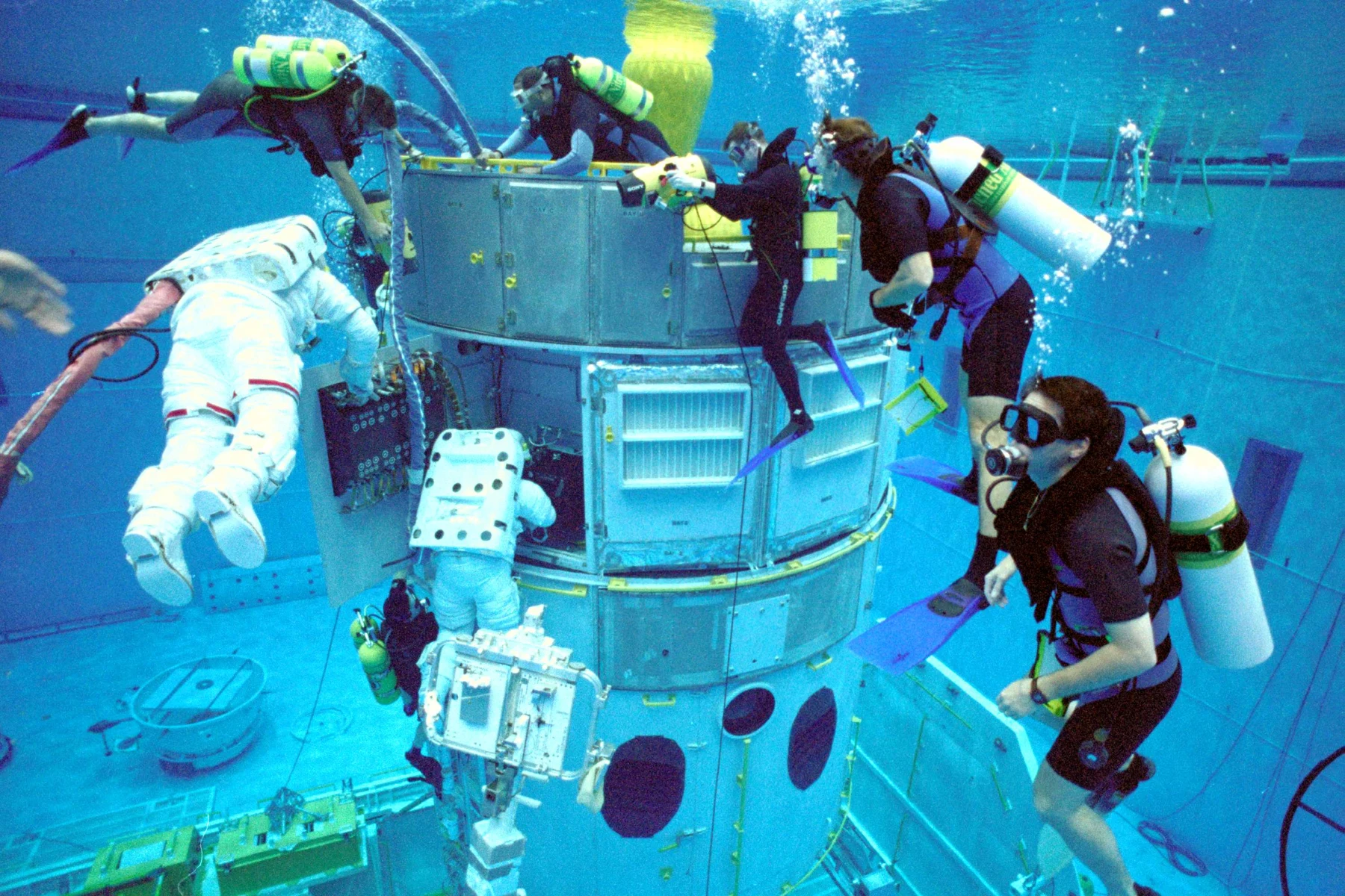 A suited astronaut and several divers work around an underwater Hubble telescope mockup.