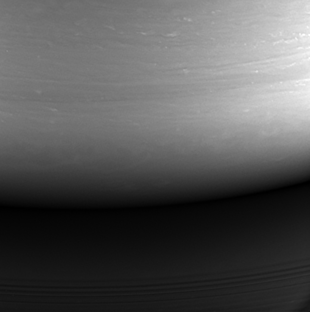 Monochrome cloud bands above Saturn’s dark curved limb, illuminated by light reflected from the rings.