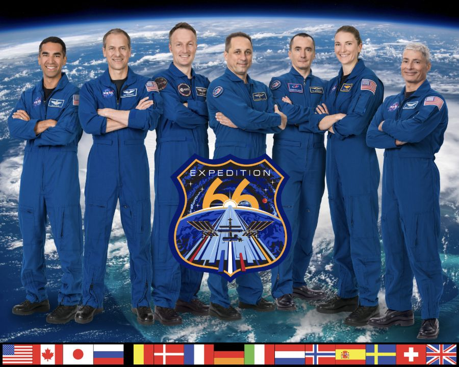Seven Expedition 66 crew members in blue flight suits pose against an Earth backdrop and expedition emblem.