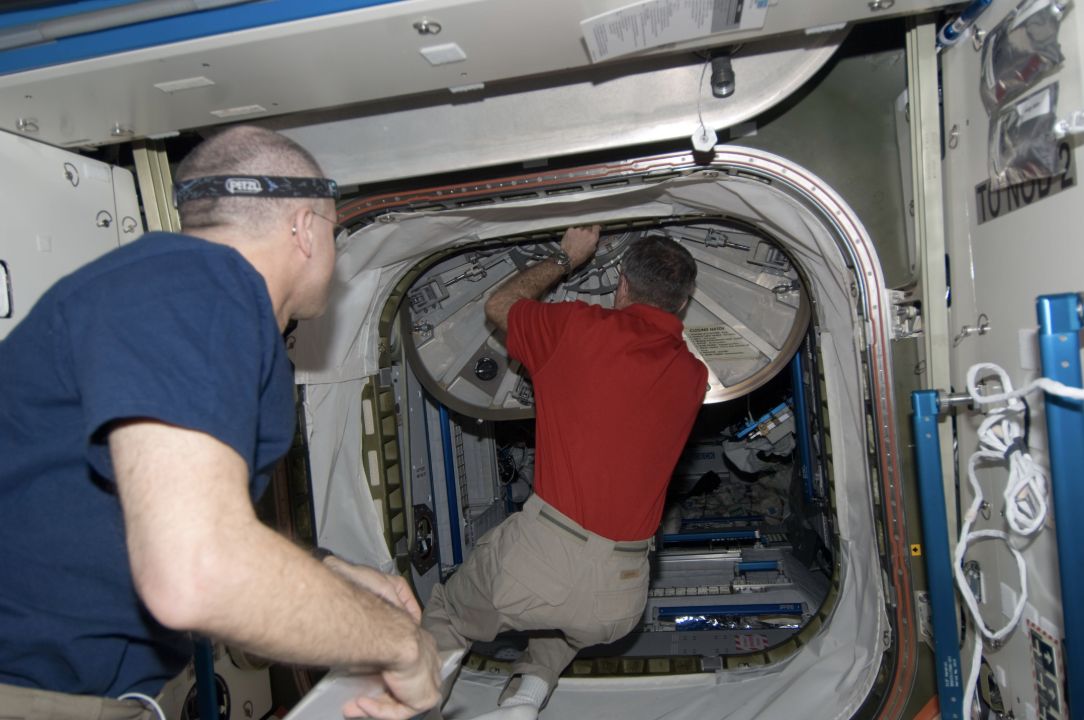 Astronaut Dan Burbank closes a hatch inside the ISS while Don Pettit watches.