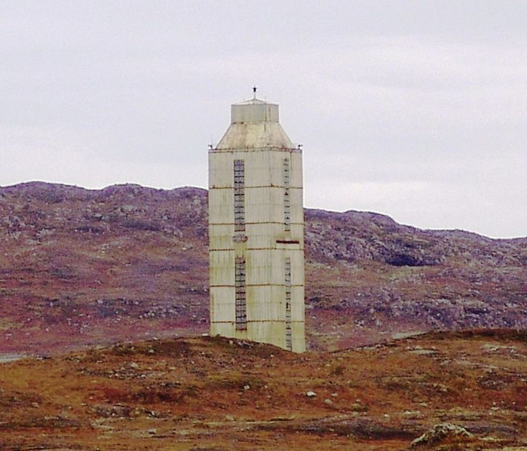 A tall pale drilling structure stands among rocky hills at the Kola site.