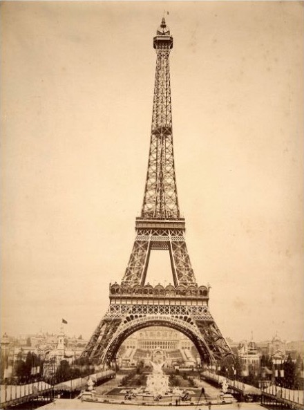 A full view of the Eiffel Tower, with fair buildings and a fountain in the foreground.