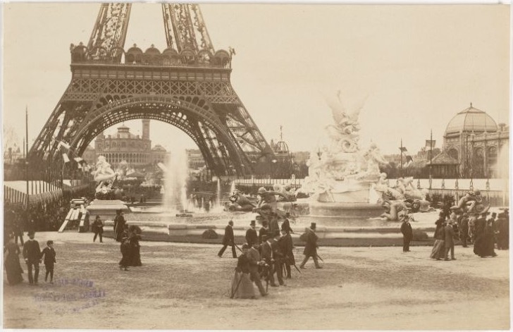 Visitors walk near a fountain beneath the tower’s lower arch at the 1889 fair.