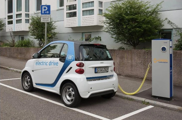 A small electric car connected by cable to a street charging station.