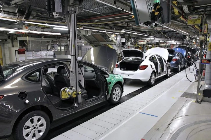 Cars at different stages of assembly on a production line inside a factory.