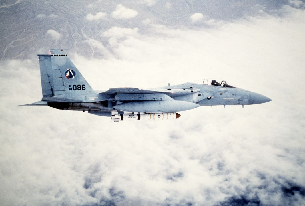 Side view of an F-15 carrying a large white missile beneath its fuselage.