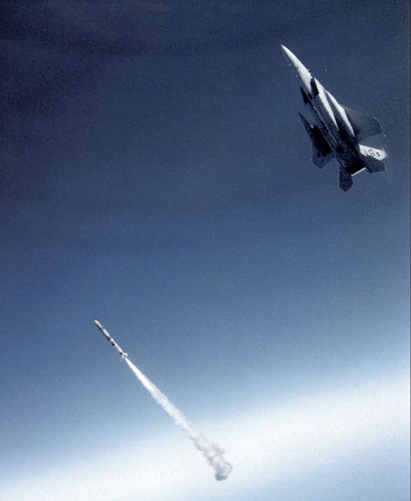 Missile trailing exhaust below an F-15 in a blue sky.