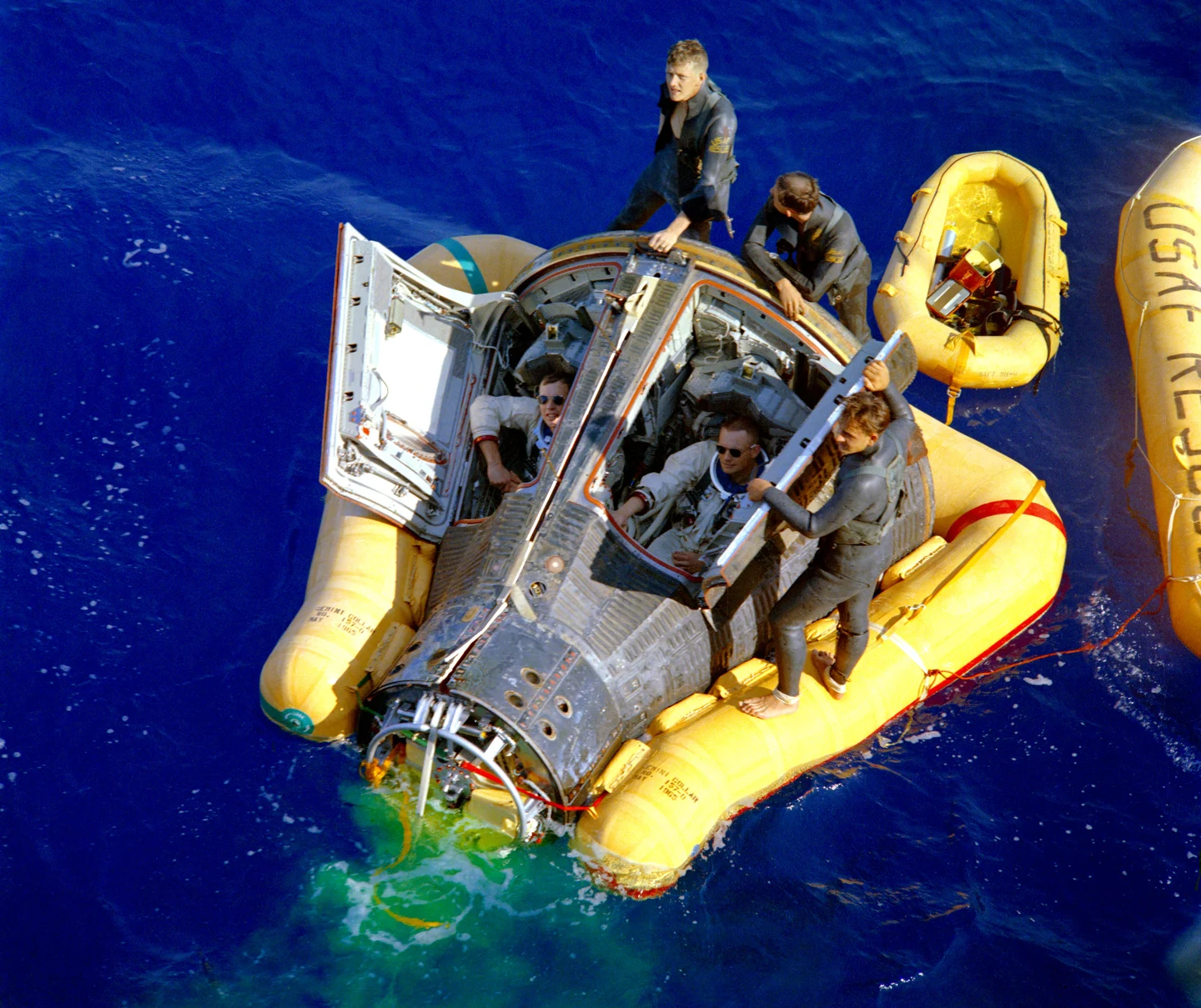 Armstrong and Scott sit in Gemini’s open hatches while three pararescuemen work around a bright yellow flotation collar in the Pacific.