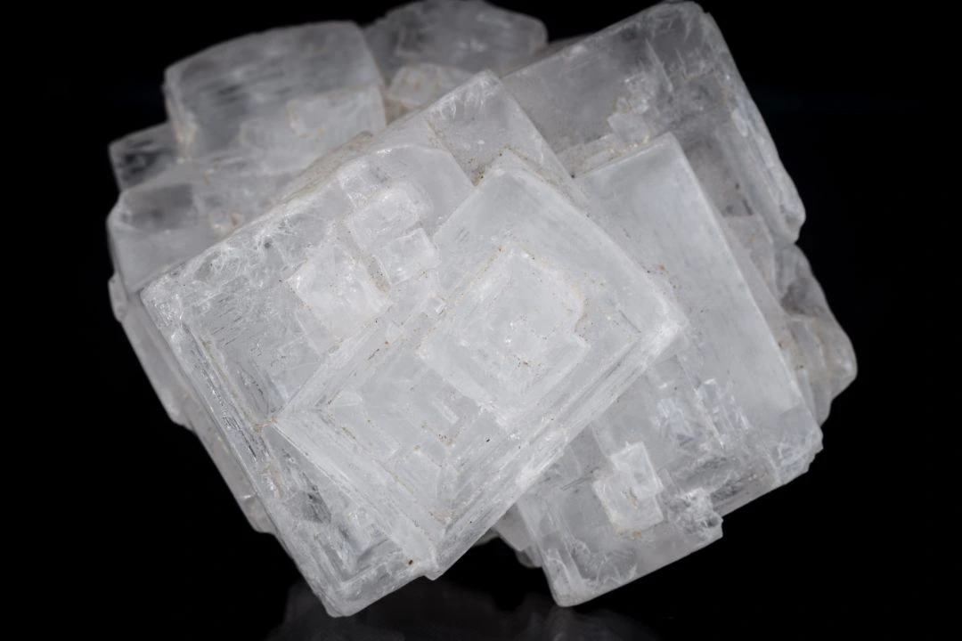 A cluster of pale translucent cubic halite crystals against a dark background.
