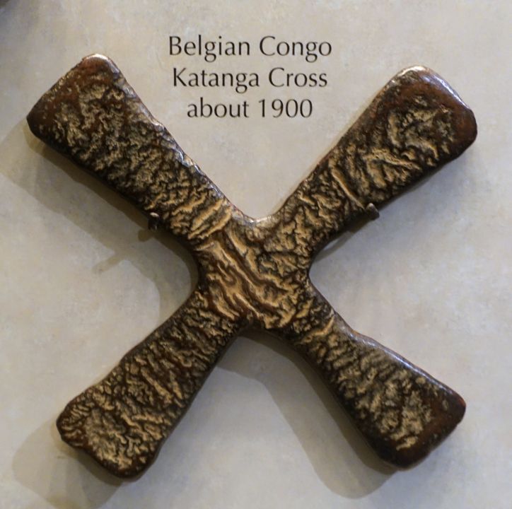 A broad, flat, cross-shaped copper object displayed on a pale background.