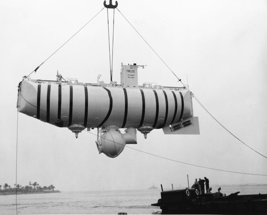 The bathyscaphe Trieste is hoisted from the water at a port, with its long float above the crew sphere.