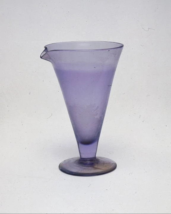 A violet, conical glass vessel with a pouring lip and a broad circular foot.