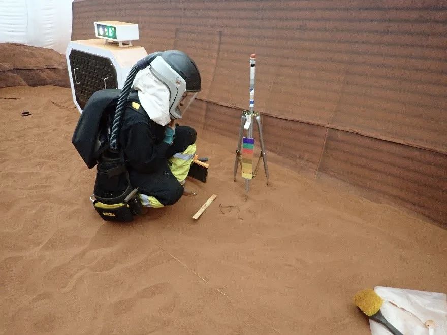 A CHAPEA crew member practices a Marswalk in an indoor red-sand test area.