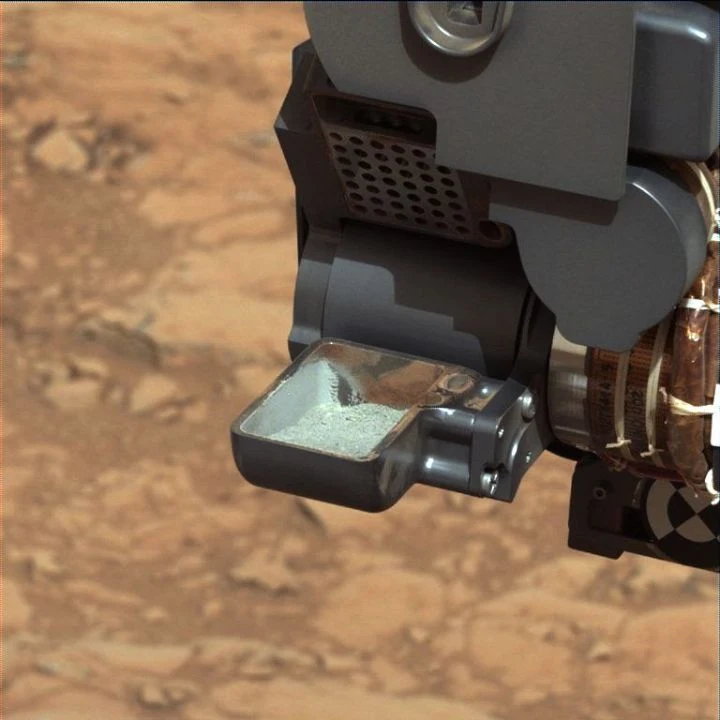 Gray-green John Klein drill powder sits in Curiosity’s scoop, with red residue on the scoop walls.