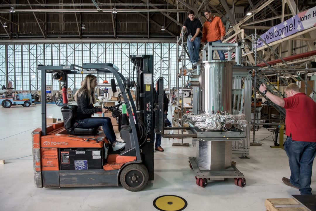 Technicians use a forklift to handle Kilopower test equipment in a hangar.