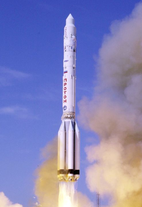 White Proton-K rocket climbing through smoke with bright exhaust.