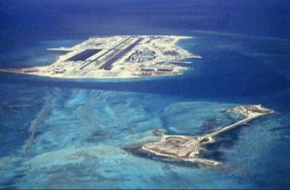 Runway and buildings on Johnston Island beside Sand Island and pale turquoise lagoon water.