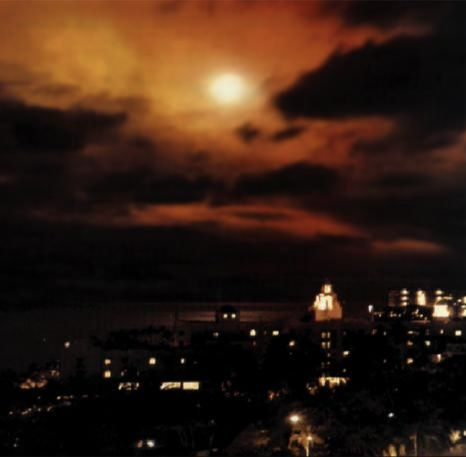 Bright orange nuclear-test glow above clouds and a city waterfront at night.