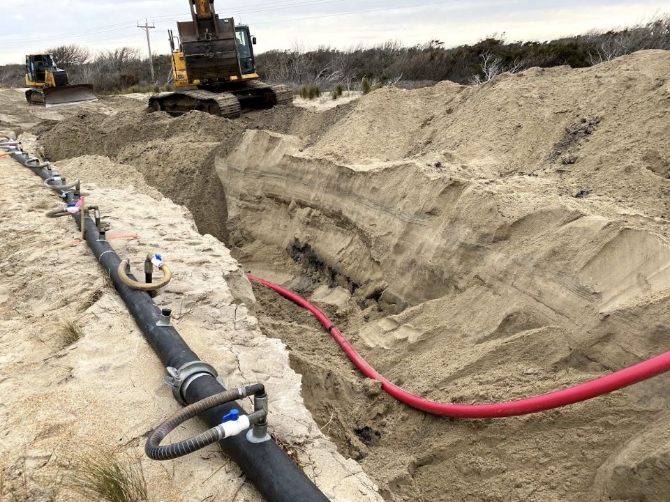 A cable in a sandy trench beside excavation equipment.
