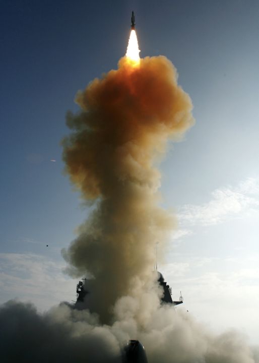 A missile rises above USS Lake Erie amid a large orange launch cloud.