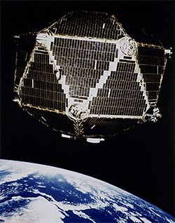 Archival illustration of a many-sided Vela 5B satellite above Earth, with its panel-covered body and projecting booms visible.
